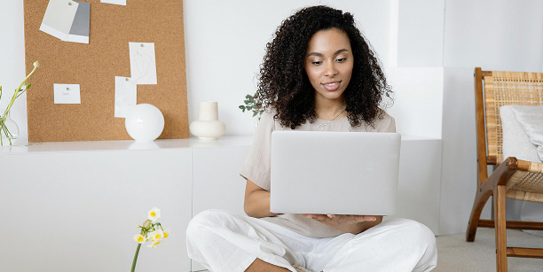 woman sitting cross legged in white office holding laptop