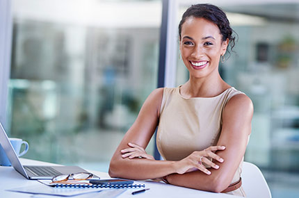 smiling woman sitting at a clean white desk with a laptop